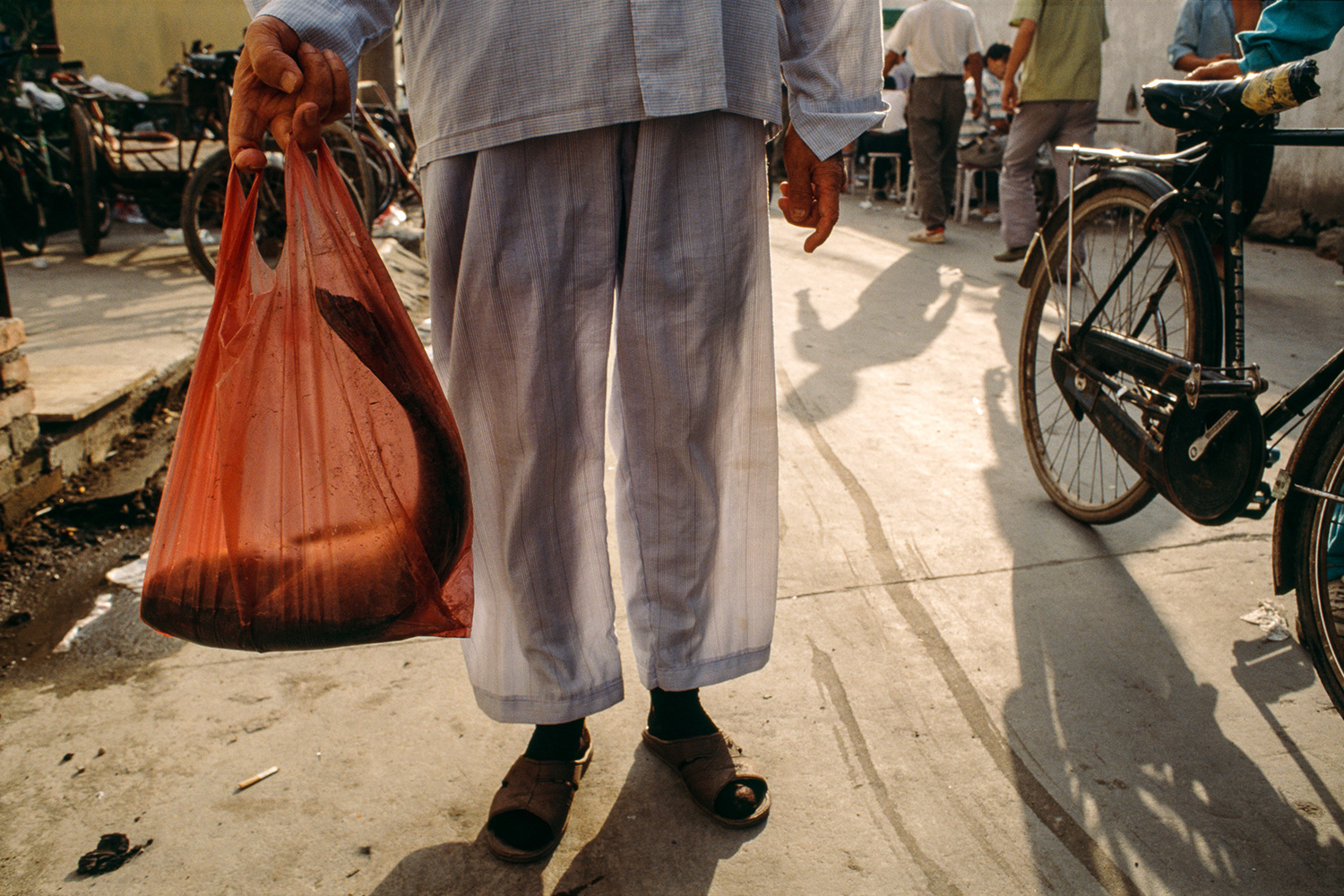 Dressed in his pajamas, a man leaves an open air market in Lujiazui with a fresh fish, 1997.