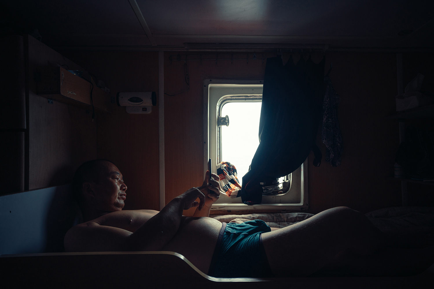 Jin reads a book on his cellphone in his cabin on Captain Xu’s ship, July 22, 2016. There is no signal when out on the water, and the narrow cabin contains no room for entertainment equipment. During his time off, Jin reads on his cellphone or sleeps.