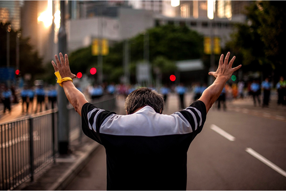 A man raises his hands toward a police line outside of the government complex. (Photo by Anthony Kwan/Getty Images)