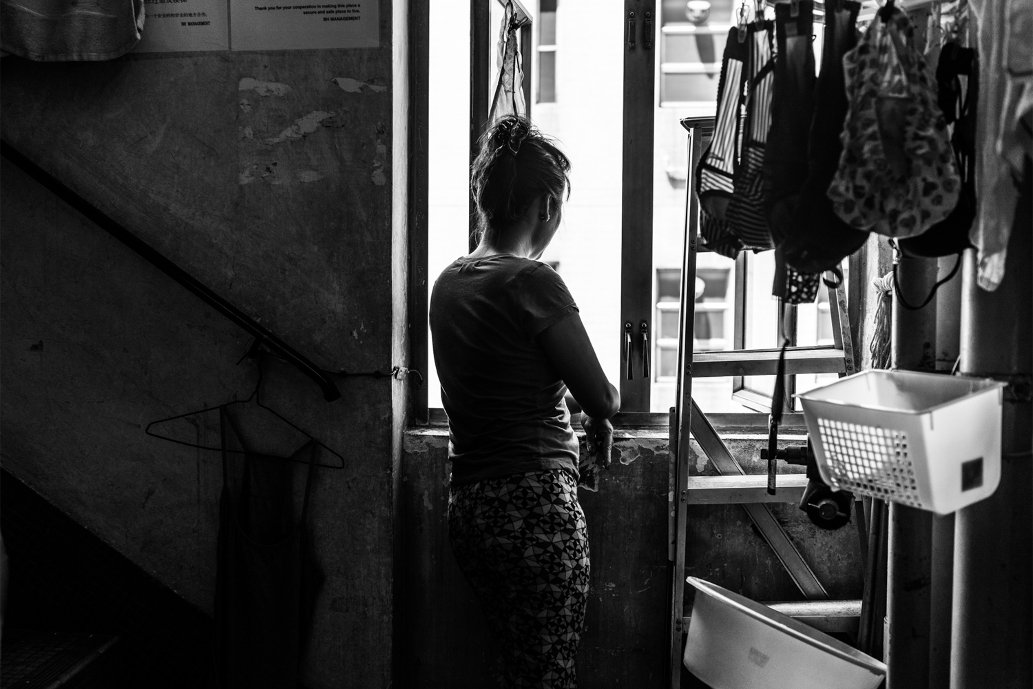 A domestic worker, who requested she not be identified, stands at the back stairway of the shelter. She was fired from her job when she complained about her sleeping situation. She had been made to sleep on the kitchen floor. The shelter is only 900 square feet, and the window in the stairway is one of the only ones in the shelter. The others are in the toilet.