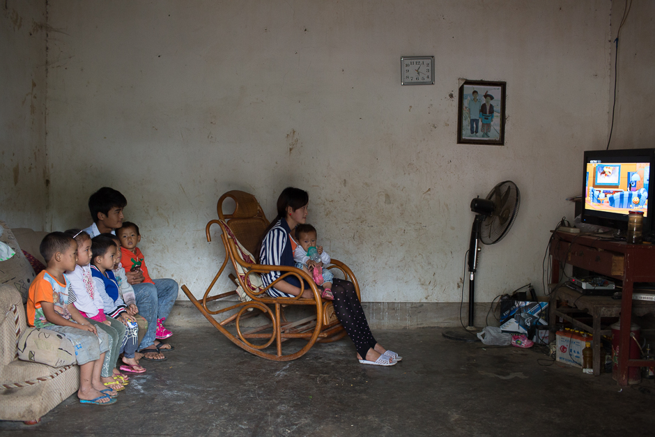 Xin, 16, holds her one-year-old daughter on her lap as she sits in a rocker watching a popular Chinese cartoon, “Big Head Son and Small Head Father,” at her home in Guangdong village, Mengla county. Xin and her husband, seated with neighborhood children on the sofa, started dating three years ago when they were in fifth grade. They dropped out of school when they got married more than a year ago.