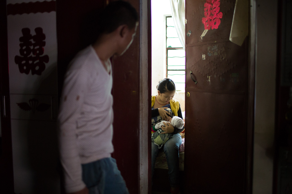 Fang, 18, looks in on his wife, Li, 16, as she nurses their one-month-old baby at home, in Guangdong village, Mengla county.