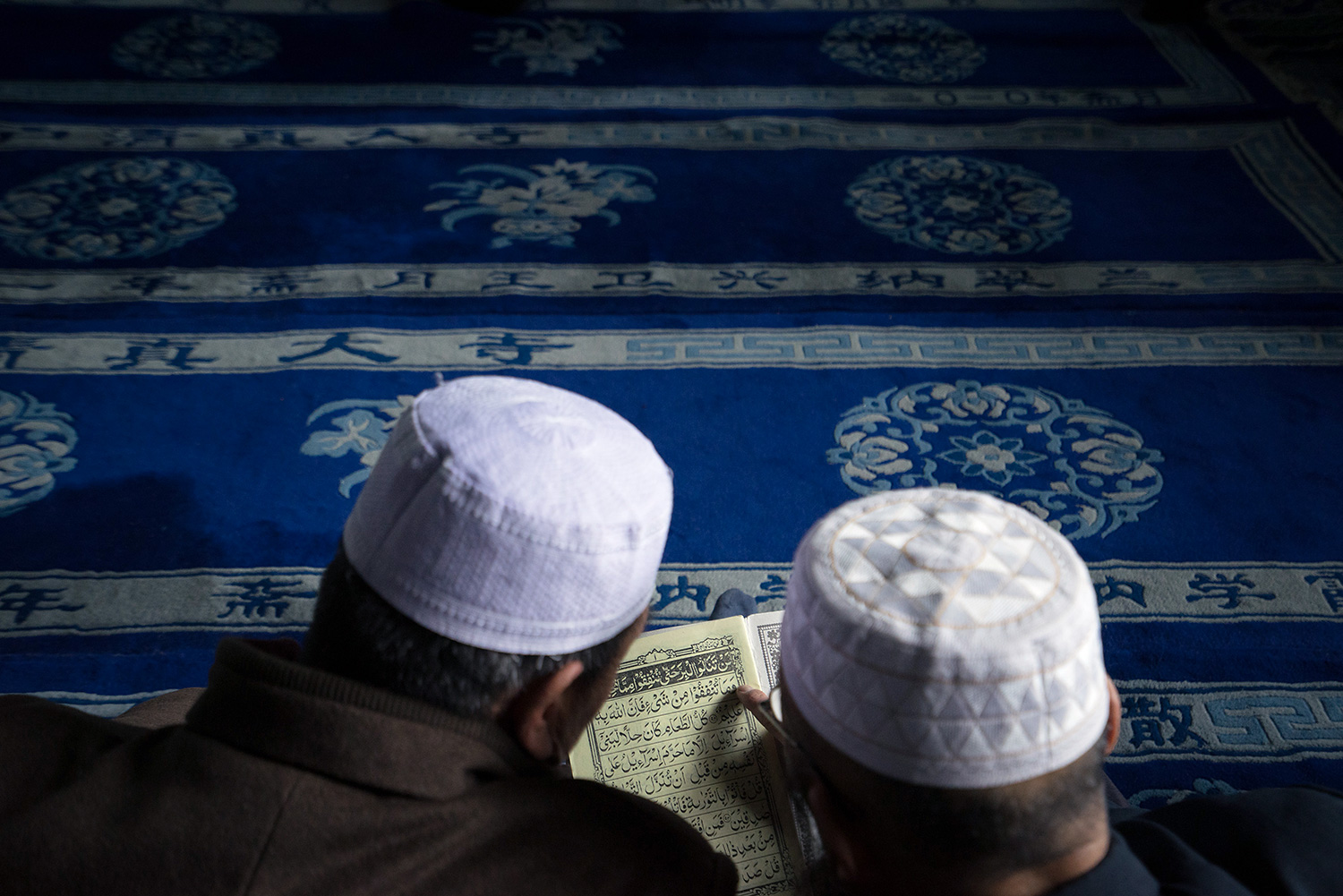 Men share a Quran while sitting on the floor in the main prayer hall of the Najiahu Mosque.