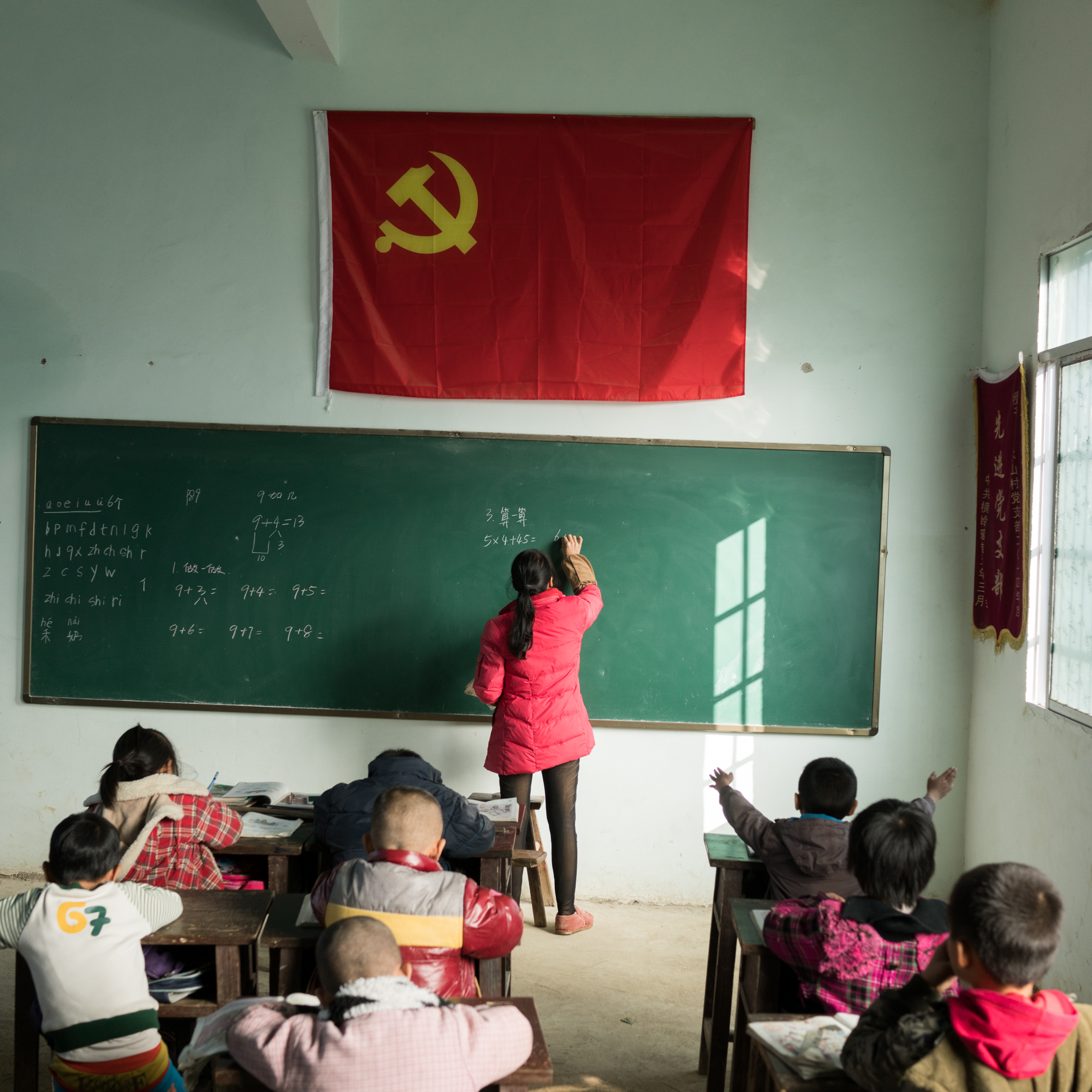 Children aged 6 to 10 sit under the Chinese Communist Party flag, learning math, in a single-room schoolhouse in Maple Wood Mountain. Just behind the school is a pit with 31 corpses, including the three children of Zhou Qun. The children were tossed into the limestone pit alongside adults who had been clubbed on the head. Everyone died over the next seven days in the pit except for Zhou. “I think of how the children died in my arms. . .” she told us, breaking down.