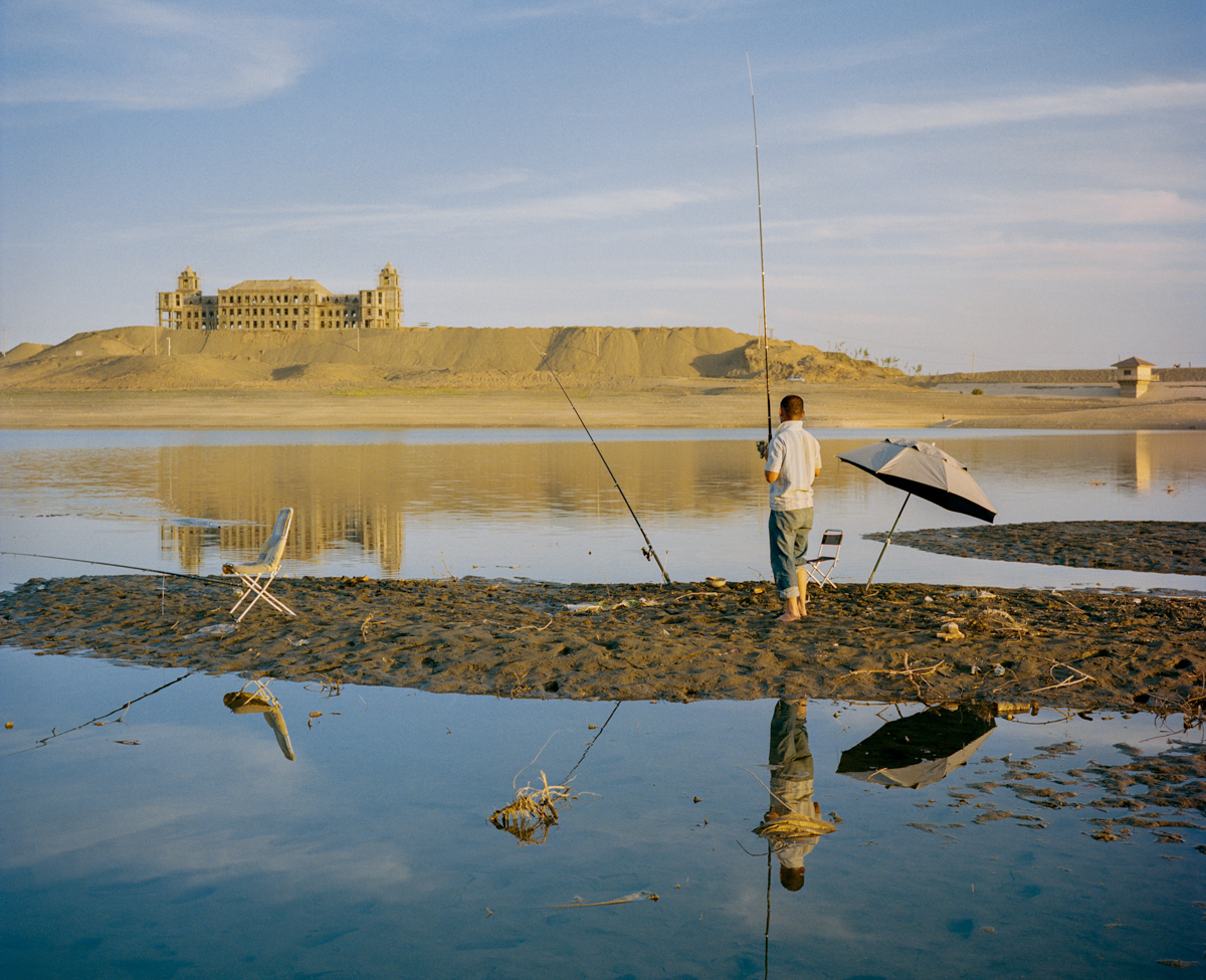 A Han migrant worker fishes on a small lake alongside an abandoned construction project on the outskirts of Turpan, June 2016.