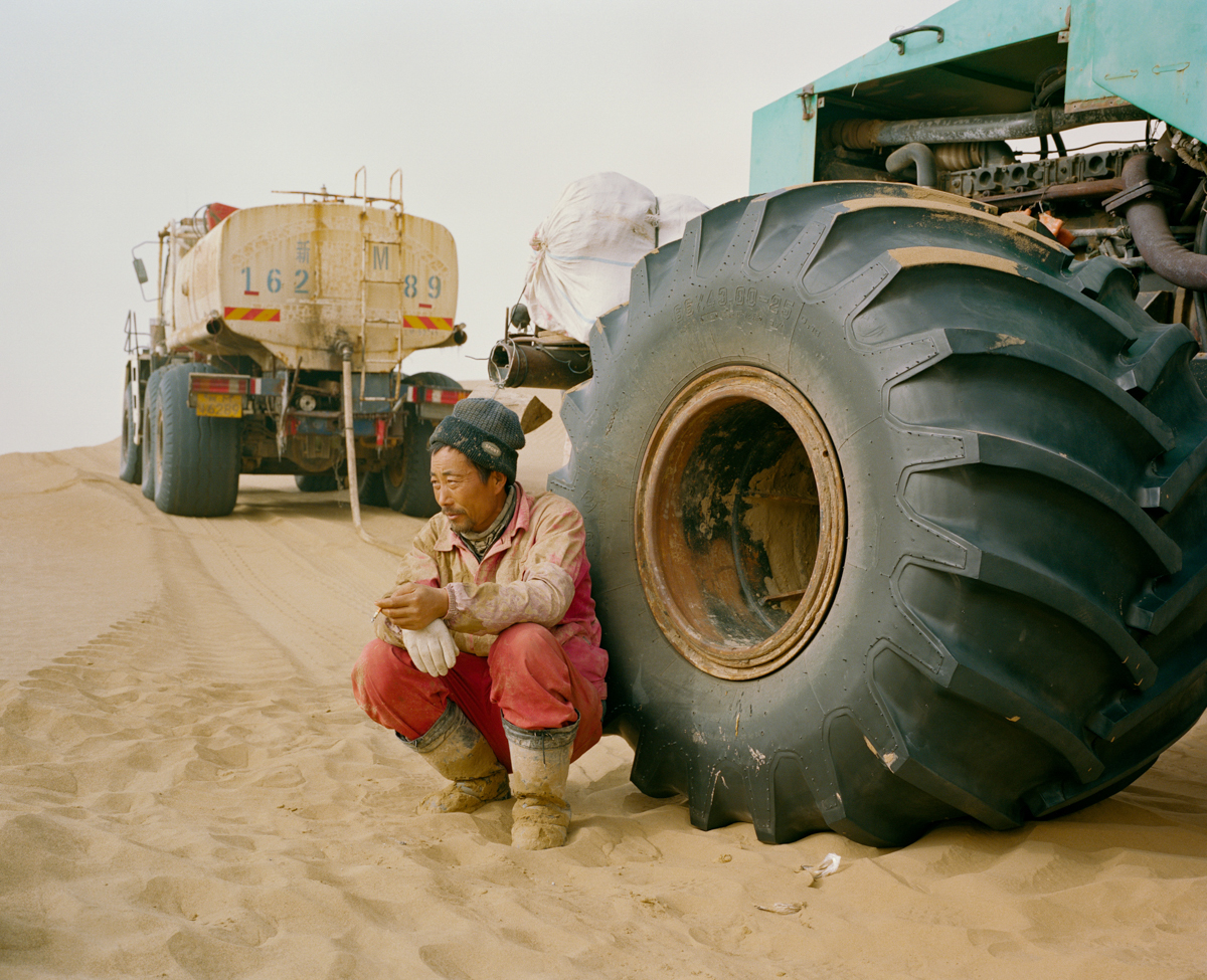A senior technician for an oil exploration team at the China National Petroleum Corporation, a Chinese state-owned enterprise, takes a cigarette break after lunch near one of the company’s vehicles, in the Taklamakan Desert, December 2016.