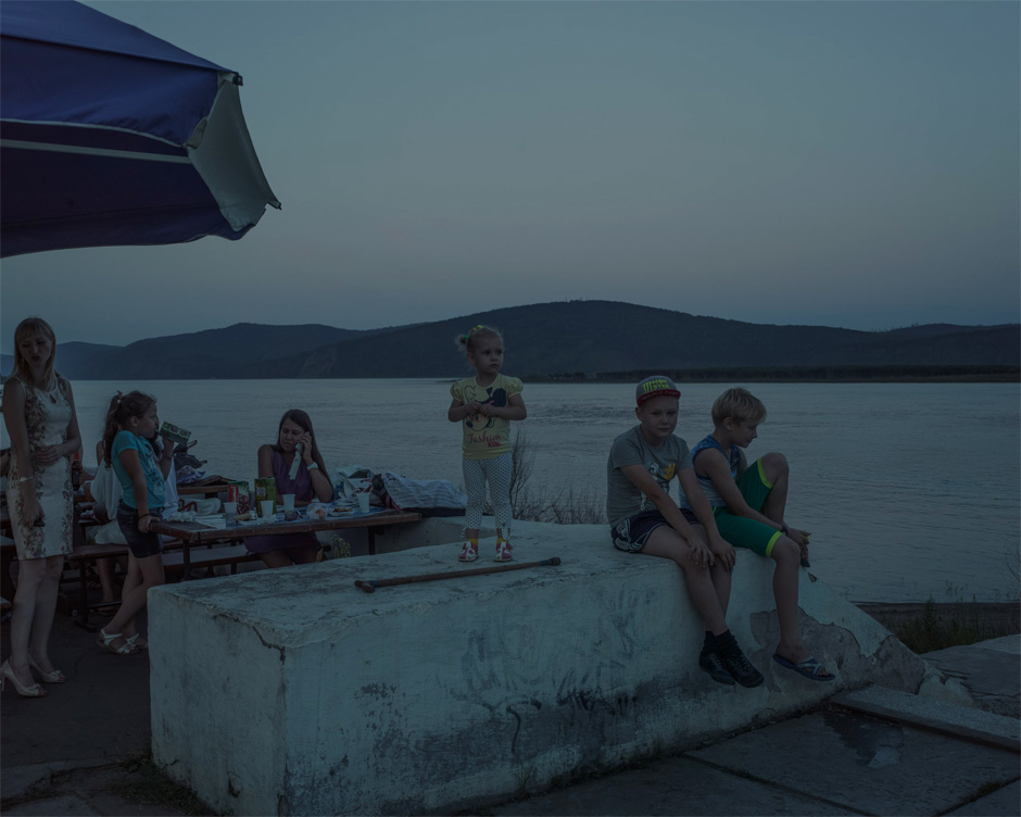A Russian family sits at a riverside café in Komsomolsk-on-Amur at dusk. The town was largely built using volunteer labor from the Communist youth organization Komsomol, hence its name. Construction of the town was aided by the use of slave labor from nearby prison camps.