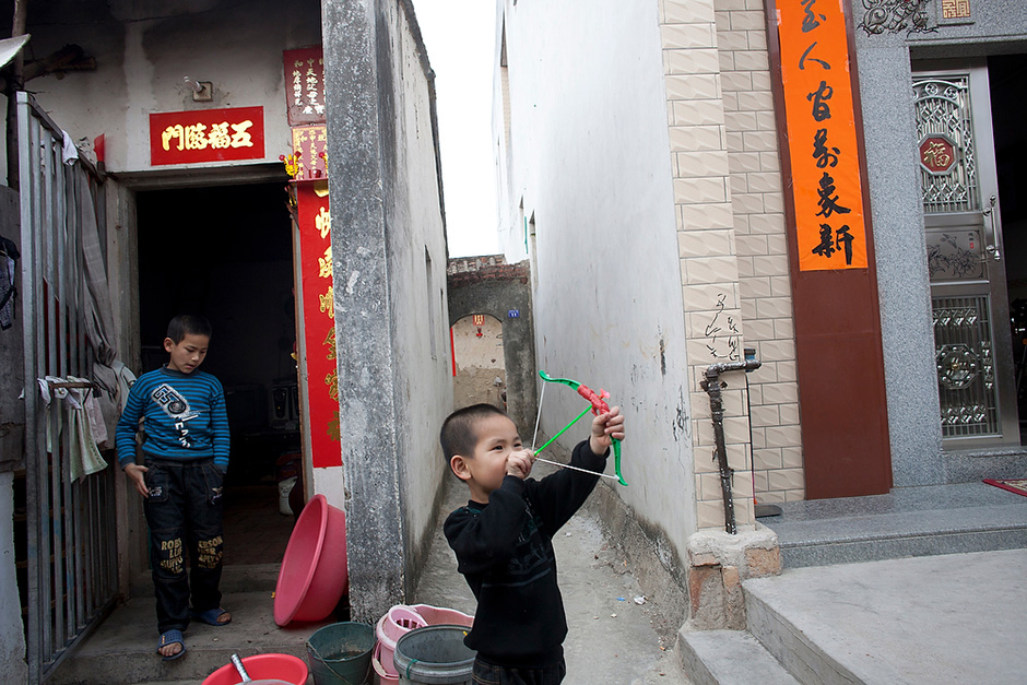 Often described as a relatively wealthy coastal Chinese village, Wukan is nevertheless divided by a visible income gap. Plush new villas stand alongside single-room homes that are crumbling and without running water. Huang Binbin, 6, pulls back on the string of a toy bow and arrow with his brother Pengpeng, 10, nearby. They live in a nine-square-meter home, at left, which they share with their parents and sister. 